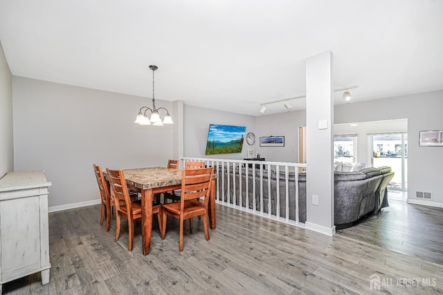 dining space featuring an inviting chandelier, track lighting, baseboards, wood finished floors, and visible vents