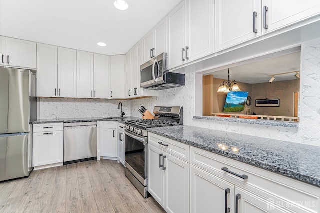 kitchen featuring decorative backsplash, a sink, a chandelier, stainless steel appliances, and white cabinetry