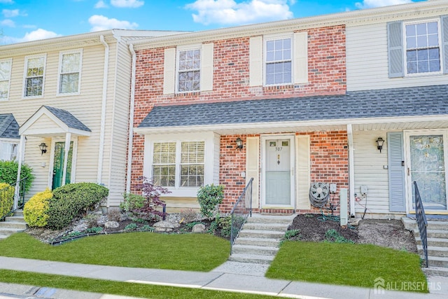 townhome / multi-family property with brick siding, a front yard, and roof with shingles