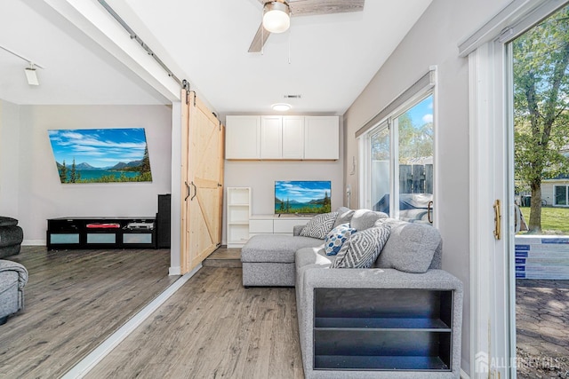 living room featuring a ceiling fan, visible vents, a barn door, baseboards, and light wood-style floors
