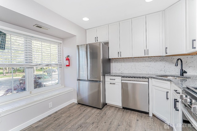 kitchen featuring light wood-style floors, white cabinets, light stone counters, a sink, and stainless steel appliances