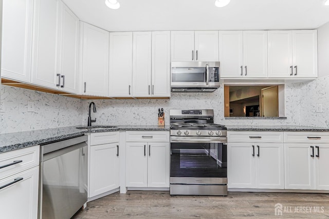 kitchen with white cabinetry, tasteful backsplash, a sink, stone counters, and appliances with stainless steel finishes