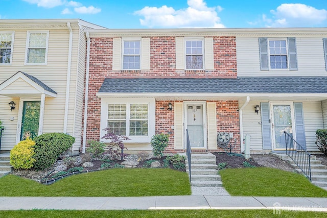 multi unit property with roof with shingles, a front lawn, and brick siding