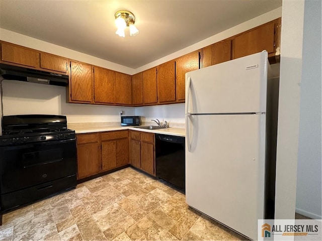kitchen featuring black appliances, under cabinet range hood, brown cabinetry, stone finish floors, and light countertops
