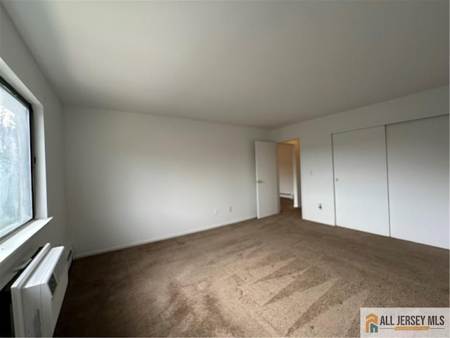 unfurnished bedroom featuring carpet, a wall mounted air conditioner, a closet, and baseboards