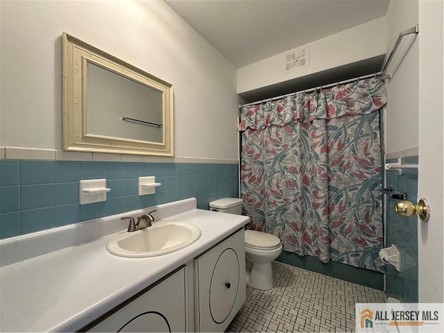 bathroom with toilet, vanity, wainscoting, tile walls, and tile patterned flooring