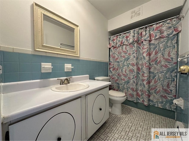 bathroom with toilet, tile walls, vanity, a wainscoted wall, and tile patterned flooring