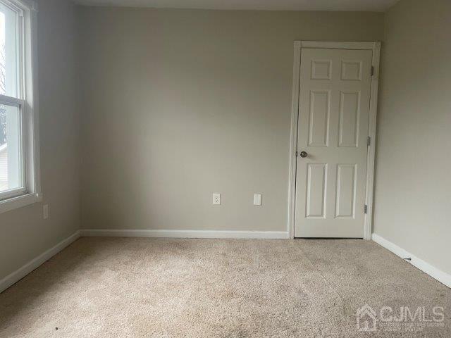 spare room featuring light carpet and baseboards