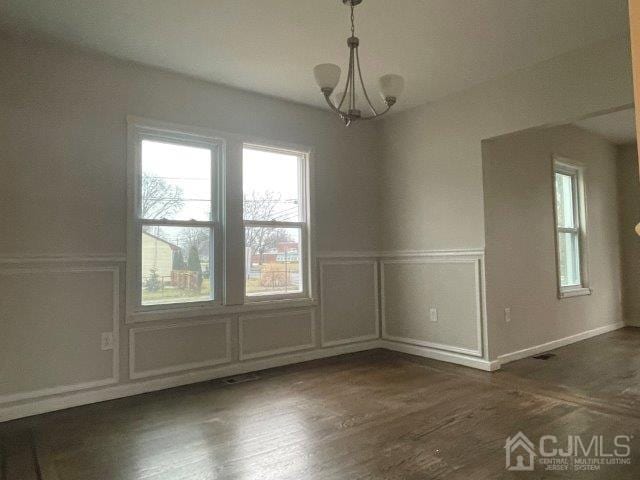 unfurnished dining area with a wainscoted wall, a chandelier, a decorative wall, and dark wood-style flooring