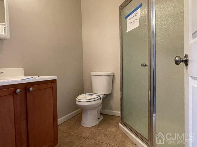 bathroom featuring toilet, vanity, baseboards, a shower stall, and tile patterned floors