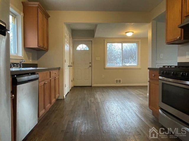 kitchen featuring dark wood-style flooring, brown cabinets, stainless steel appliances, dark countertops, and visible vents