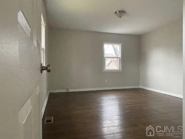 unfurnished room featuring visible vents, baseboards, and dark wood-type flooring