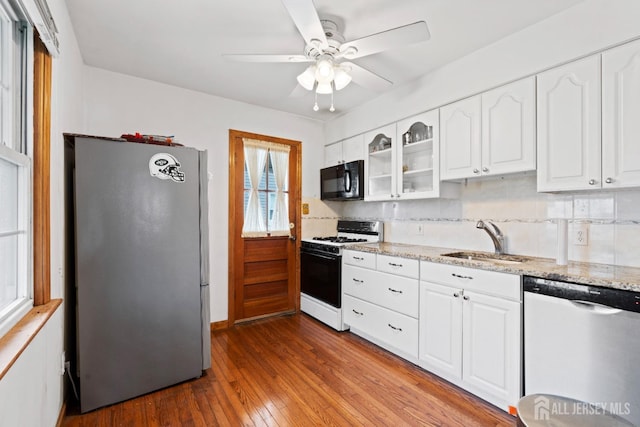 kitchen featuring appliances with stainless steel finishes, a sink, hardwood / wood-style floors, light stone countertops, and decorative backsplash