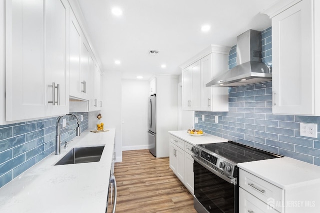 kitchen with electric stove, sink, white cabinets, and wall chimney range hood