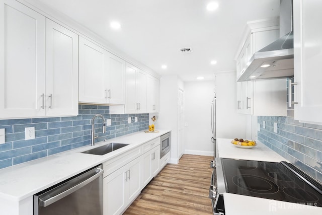 kitchen with stainless steel appliances, sink, wall chimney range hood, light hardwood / wood-style flooring, and white cabinets