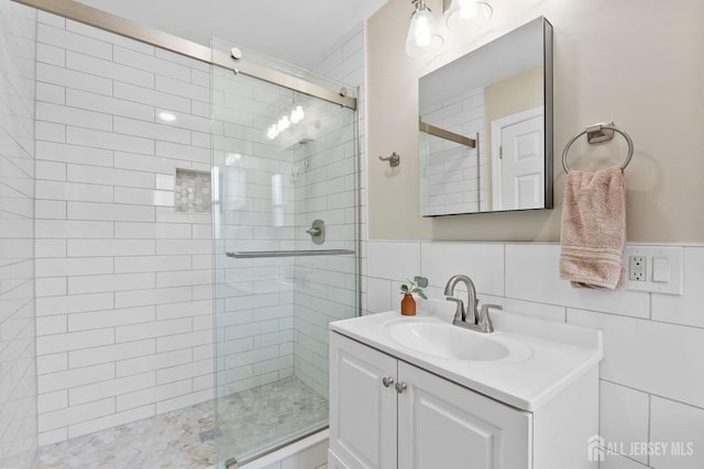 full bath featuring tile walls, a shower stall, vanity, and a wainscoted wall