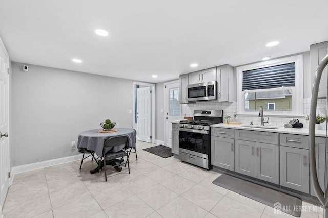 kitchen with light countertops, a sink, stainless steel appliances, gray cabinetry, and baseboards