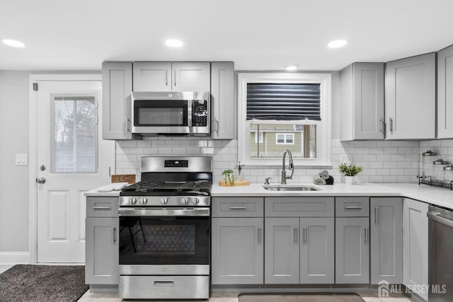kitchen with a sink, gray cabinets, backsplash, and appliances with stainless steel finishes