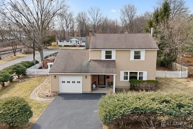 traditional home featuring an attached garage, a shingled roof, driveway, and fence