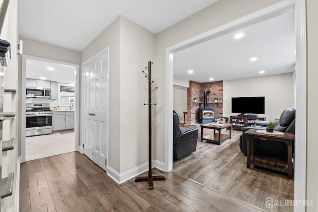 living room with a wood stove, recessed lighting, wood finished floors, and baseboards