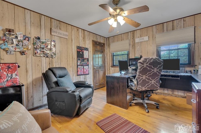 home office featuring ceiling fan, wooden walls, light wood-type flooring, and plenty of natural light