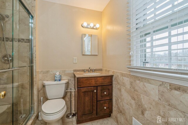 bathroom with tile walls, vanity, toilet, and walk in shower