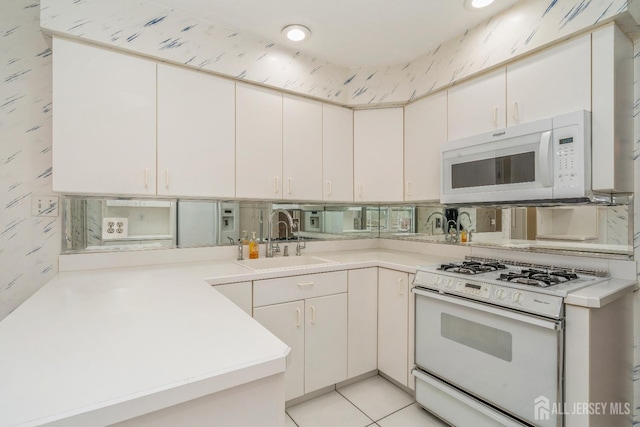 kitchen with sink, white appliances, white cabinetry, light tile patterned flooring, and kitchen peninsula