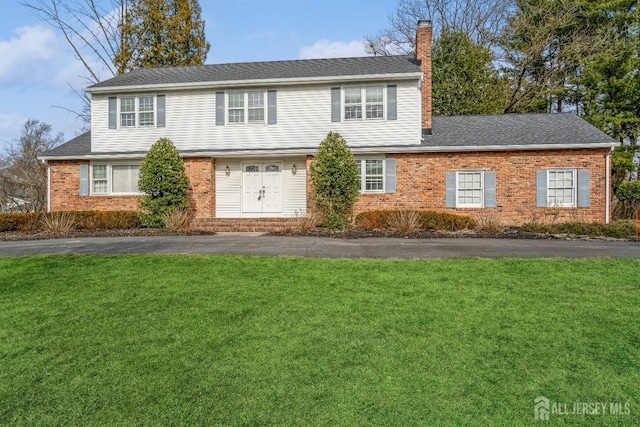 view of front of property with brick siding, a shingled roof, aphalt driveway, a front yard, and a chimney