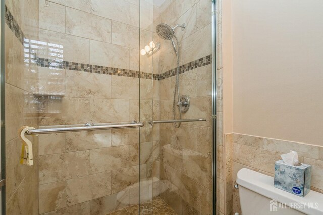 bathroom featuring toilet, a shower with door, and tile walls