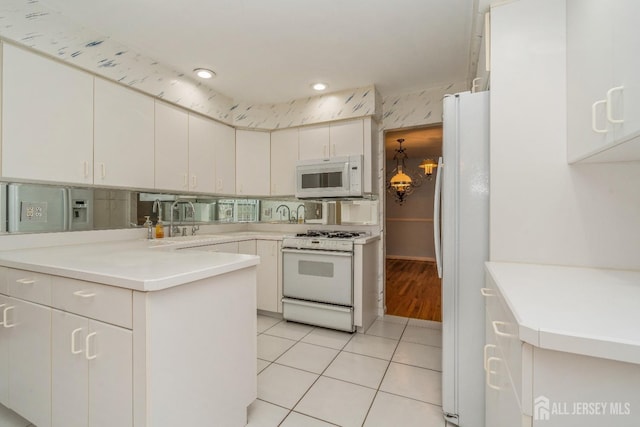 kitchen featuring sink, white cabinetry, light tile patterned floors, kitchen peninsula, and white appliances