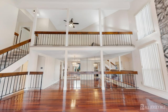 living area with stairway, high vaulted ceiling, wood finished floors, and ceiling fan with notable chandelier