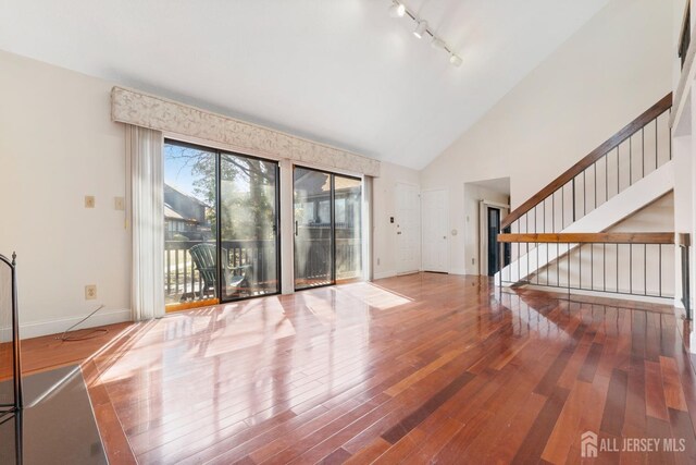 unfurnished living room with stairway, baseboards, high vaulted ceiling, hardwood / wood-style flooring, and track lighting