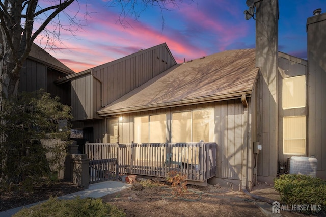 rear view of property with a chimney, central AC, a deck, and roof with shingles