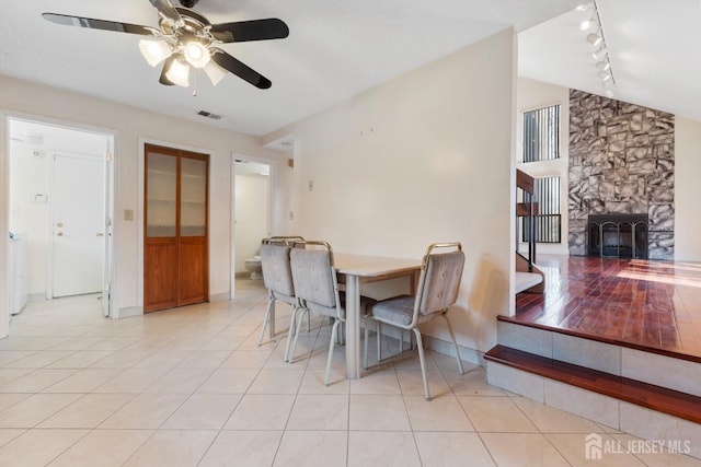 dining space with a stone fireplace, lofted ceiling, light tile patterned flooring, and visible vents