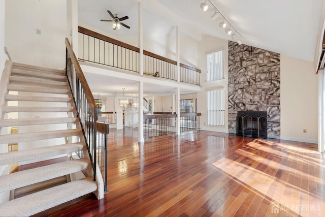 unfurnished living room featuring baseboards, stairway, hardwood / wood-style floors, ceiling fan with notable chandelier, and a fireplace