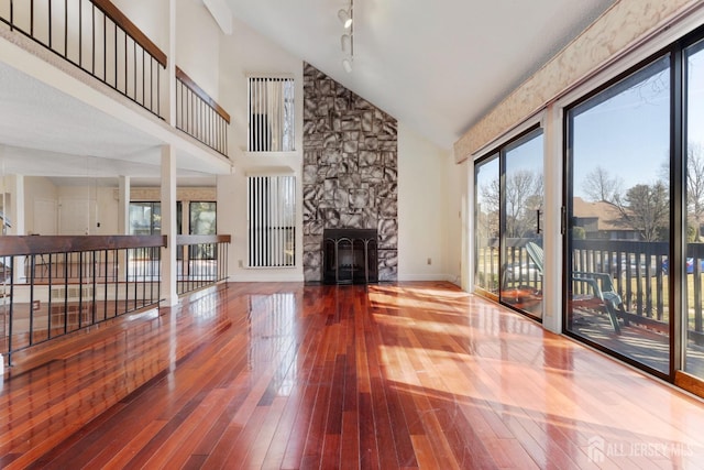 living area featuring a fireplace, high vaulted ceiling, baseboards, and wood-type flooring