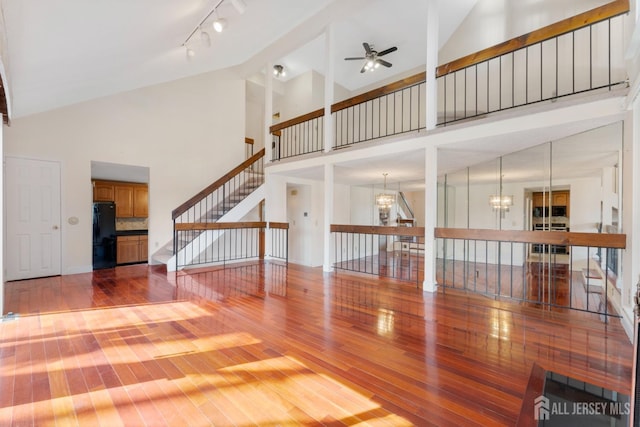 unfurnished living room with ceiling fan with notable chandelier, high vaulted ceiling, stairs, and hardwood / wood-style floors