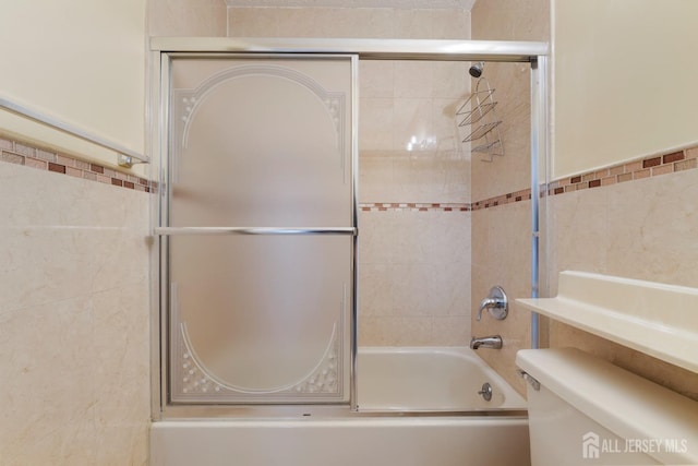 bathroom featuring toilet, tile walls, and shower / bath combination with glass door