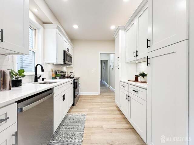 kitchen with sink, white cabinetry, light hardwood / wood-style floors, decorative backsplash, and appliances with stainless steel finishes