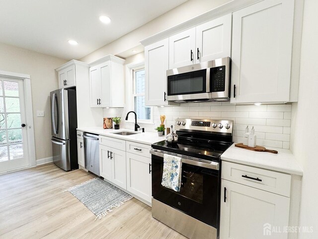 kitchen with white cabinets, light hardwood / wood-style floors, stainless steel appliances, sink, and backsplash