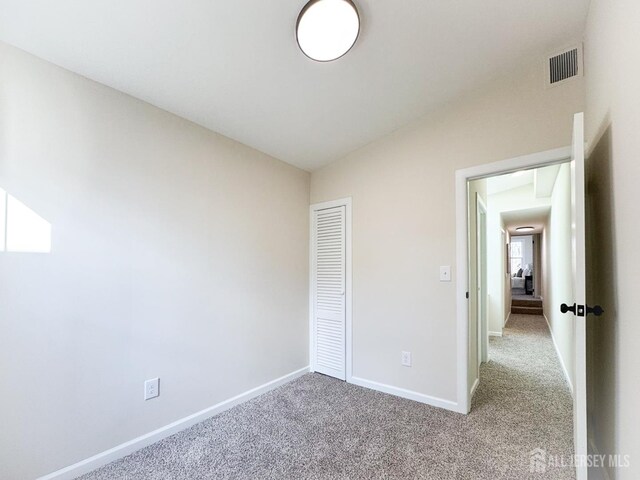 unfurnished bedroom with lofted ceiling, a closet, and light carpet