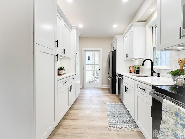 kitchen with sink, white cabinetry, light wood-type flooring, tasteful backsplash, and appliances with stainless steel finishes