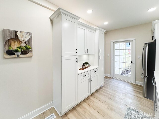 interior space featuring stainless steel refrigerator, white cabinets, backsplash, and light hardwood / wood-style flooring