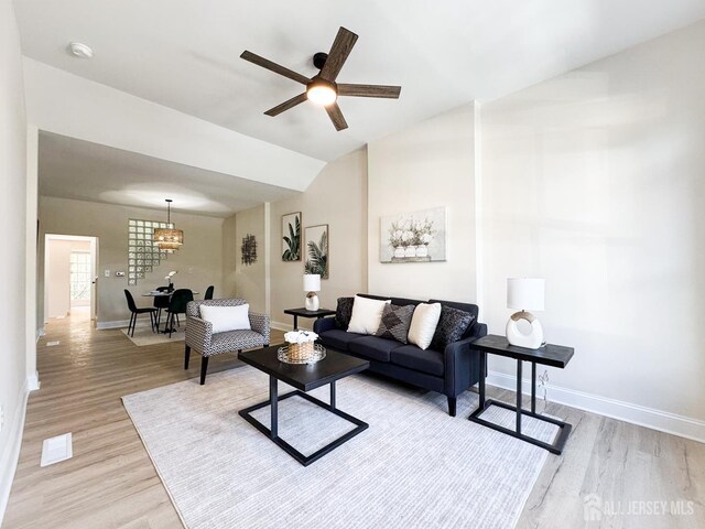 living room with ceiling fan with notable chandelier, light wood-type flooring, and lofted ceiling