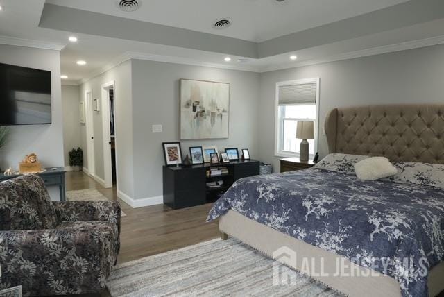 bedroom with hardwood / wood-style flooring, crown molding, and a raised ceiling