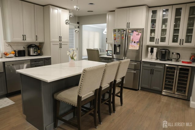 kitchen featuring decorative light fixtures, a kitchen island, appliances with stainless steel finishes, white cabinets, and beverage cooler