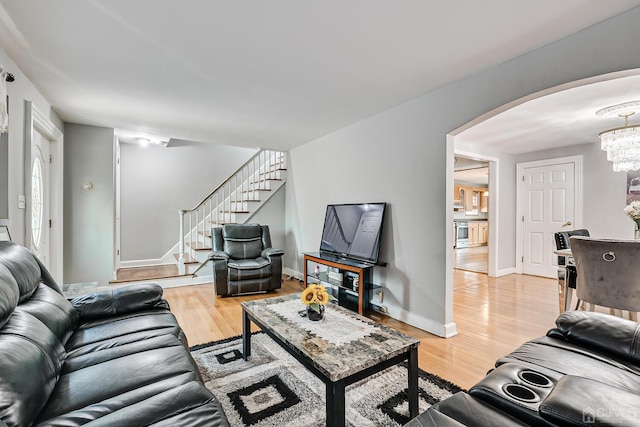 living area with baseboards, light wood-type flooring, stairs, an inviting chandelier, and arched walkways