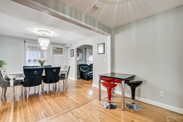 dining area with baseboards, a chandelier, hardwood / wood-style flooring, arched walkways, and a wall mounted AC