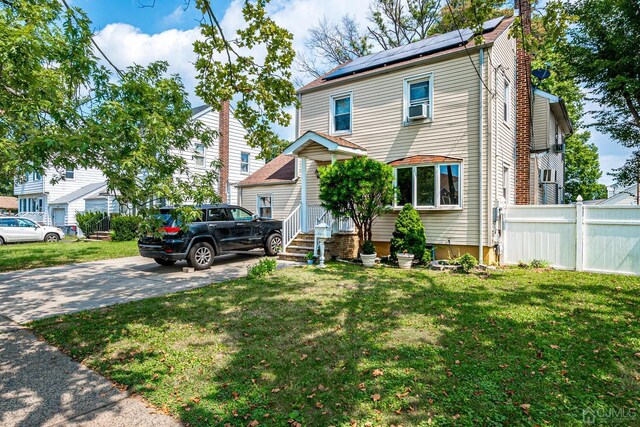 view of front of property featuring cooling unit, a front lawn, and solar panels