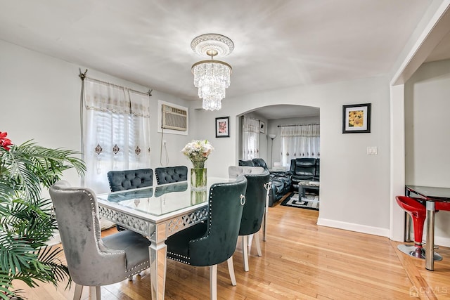 dining area featuring a wall mounted air conditioner, light wood-type flooring, arched walkways, baseboards, and a chandelier